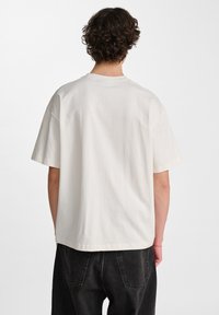 Witte, korte mouwen t-shirt van gladde katoen. Heeft een ontspannen pasvorm en een subtiele textuur. Achteraanzicht toont een ronde hals en brede schouders.