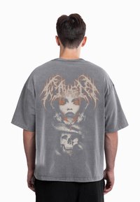T-shirt cinzenta oversize com um grande gráfico de um rosto e crânio nas costas. O design inclui detalhes em laranja e um acabamento texturizado.
