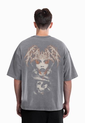 Grå oversized t-shirt med en stor grafik af et ansigt og en kranium på ryggen. Designet inkluderer orange accenter og en tekstureret finish.