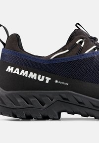 Nahaufnahme eines dunkelblauen und schwarzen Mammut Gore-Tex Wanderschuhs mit strukturiertem Sohlenprofil und Zugschlaufe an der Ferse vor weißem Hintergrund.