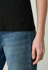 Zwarte katoenen T-shirt met een ronde rubberen logopatch en een rechte zoom, gecombineerd met lichtblauwe denim jeans met een gestructureerde afwerking.