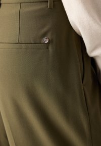 Oliwkowe spodnie wykonane z fakturowanej tkaniny, z tylną kieszenią i srebrnym akcentem metalowym.