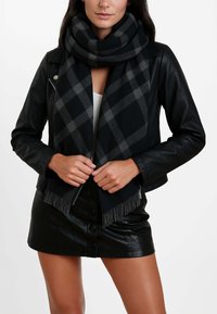 Sciarpa a quadri nera e grigia realizzata in tessuto morbido, con frange alle estremità. Indossata con una giacca di pelle nera e una gonna, accentuando un look a strati.