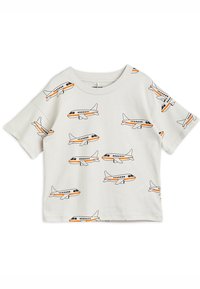 Camisa blanca de manga corta con un gráfico de avión repetido en negro y naranja. Tejido de algodón suave, cuello redondo, ajuste relajado.