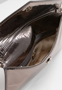 Sac à main rose métallisé avec une finition lisse et brillante. Comprend une poche zippée et un intérieur beige avec un motif de logo répété.