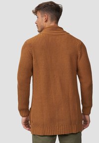 Strik cardigan i rustfarve med et struktureret mønster, lange ærmer og sjalskrave. Har ribbede manchetter og kant.