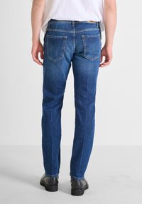 Blue denim jeans with a straight leg cut, featuring a mid-rise waist, five pockets, and subtle stitching details. Worn with black boots.