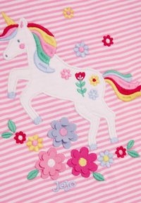 Valkoinen broderad enhörning med regnbågshår på rosa randig tyg, omgiven av flerfärgade blommor och texten "Jojo."