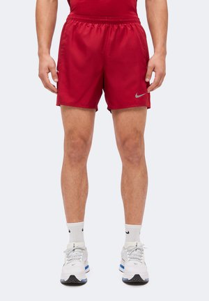 Homme portant un short de sport rouge avec un logo Nike gris, des chaussettes Nike blanches et des chaussures de sport blanches avec des touches bleues et noires.