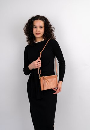 Tan læder crossover taske med lynlåslukning, frontlomme og justerbar rem, vist mod en ensfarvet hvid baggrund.
