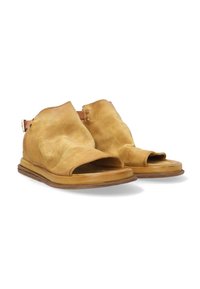 Tan leather sandals with open-toe design, ankle strap, and a flat sole. The texture is slightly wrinkled, showcasing a natural finish.