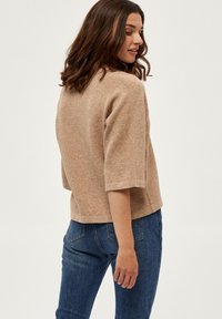 Beige sweater med en tekstureret overflade, der har trekvartærmer og en afslappet pasform, parret med mørkeblå denimjeans.
