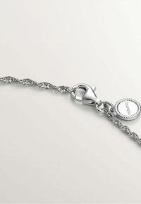 Pulsera de cadena de plata con eslabones retorcidos, que cuenta con un cierre de langosta y un charm redondo con detalle de borde de cuerda.