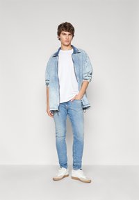 Ljusblå denimjacka med en mörkare krage, vit t-shirt, ljusblå jeans och vita sneakers med beiga detaljer. Avslappnad klädsel.
