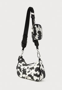 Bolso de mano con estampado de vaca en blanco y negro, con forma curva, cierre de cremallera, correa ajustable y un pequeño monedero desmontable. Texture suave.