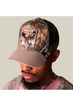 Hombre que lleva una gorra de béisbol de camuflaje con un parche de águila con la etiqueta "REPRESENT" en la parte delantera, cubriendo parcialmente sus ojos.