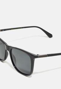 Ochelari de soare polarizați negri cu lentile întunecate, rame dreptunghiulare, accente metalice texturate pe brațe și un design elegant din plastic mat.