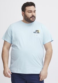 Světle modré bavlněné tričko s kulatým výstřihem, na levé hrudi má černý a žlutý motiv palmy a slunce. Krátké rukávy.
