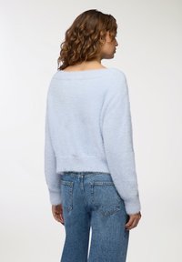 Maglione azzurro chiaro, soffice, con un design off-the-shoulder e maniche lunghe, abbinato a jeans di denim a vita alta. Texture morbida e vestibilità corta.
