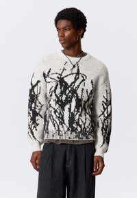 Dundi kötött pulóver krém színben, fekete absztrakt mintákkal. Lazább fazonú, kör alakú nyakkivágással és bordázott mandzsettákkal rendelkezik.