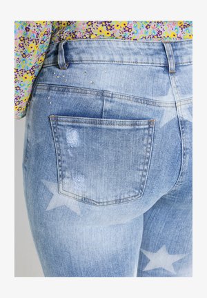 Helle blaue Jeans im Denim-Stil mit einem verblassten Sternmuster, ausgefransten Details und dezenten Strassakzenten in der Nähe der Gesäßtasche.