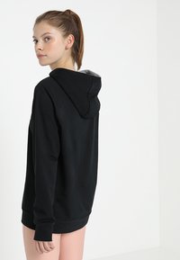 Svart hoodie med fodrad insida, har en dragsko i huvan, ribbade muddarna och nederkant. Slät tyg, avslappnad passform, tillsammans med rosa randiga byxor.