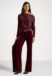 Burgundowy satynowy top z asymetrycznym, jedno-ramiennym krojem, zestawiony z szerokimi spodniami z sztruksu. Czółenka w kolorze czarnym dopełniają stylizację. Widoczny jest detal złotej klamry paska.