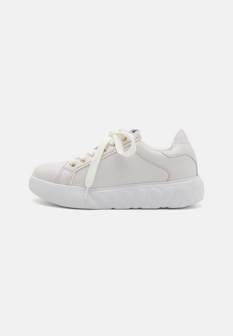 White sneaker with a smooth leather upper, round toe, gold eyelets, and flat laces. Features a thick white rubber sole with a textured design.