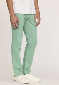 Pantalons en coton vert menthe à coupe Slim, avec une texture lisse et des détails de couture subtils, associés à des baskets blanches.