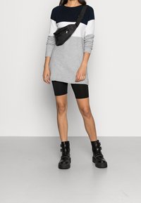 Vestito in maglione grigio con righe blu navy e bianche, abbinato a pantaloni ciclismo neri e stivaletti chunky neri alla caviglia. Marsupio indossato a tracolla.