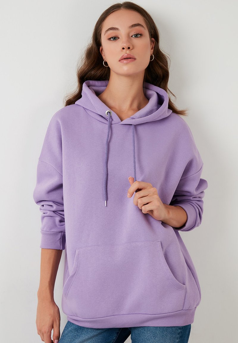 Sudadera grande morada con capucha ajustable, bolsillo frontal, puños acanalados y dobladillo. Material suave con una textura lisa.