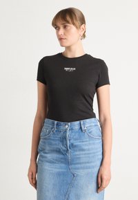 Černé bavlněné tričko s krátkým rukávem, se bílým logem "TOMMY JEANS". V kombinaci se světle modrou džínovou sukní s jemným švem.