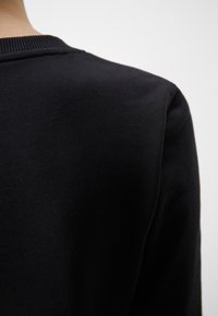 Sudadera negra con cuello acanalado y una tela suave y texturizada. La imagen se centra en la parte trasera, mostrando una silueta suave.