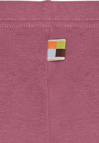 Tessuto rosa con una texture liscia, caratterizzato da un piccolo etichetta con un motivo a quadri multicolori sul lato superiore.