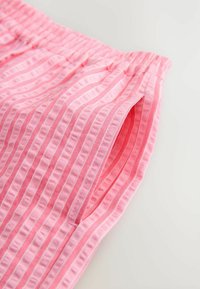 Roze elastische taillebroek met verticale ribbelstructuur en zijzakken. De stof heeft afwisselende gladde en gestructureerde strepen.