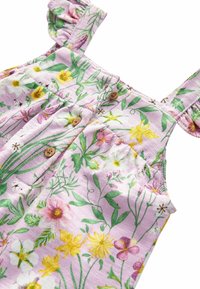 Prenda floral con fondo rosa, que presenta hojas verdes y flores amarillas, moradas y blancas. Incluye botones de madera y tirantes con volantes.
