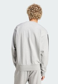 Lys grå sweatshirt med rund hals, har lange ærmer og ribbede manchetter, lavet af blødt, tekstureret stof. Ingen synlig branding.