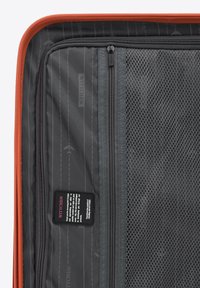 Oranžový kufr s šedými síťovanými kapsami, značkovými štítky a vzorem letadel. Obsahuje zipové uzávěry a odolnou tkaninu.