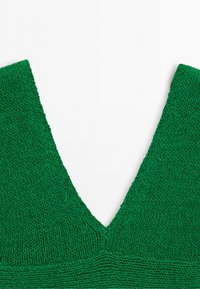 Close-up of green knitted fabric with a deep v-shaped neckline and a textured pattern near the bottom edge.