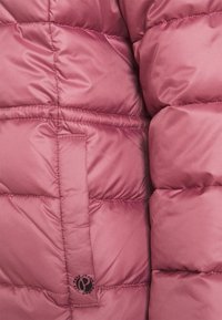 Sección de chaqueta acolchada rosa con una textura suave y brillante, diseño acolchado y un parche de logo en el lateral.