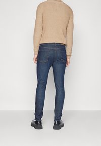 Mörkblå denimjeans med slim fit, med vanliga bakfickor och subtila sömnadsdetaljer. Matchad med en beige ribbad tröja.