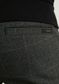 Rutig svarta och grå byxor med en slät textur, med en bakficka och en liten "CHASIN'" etikett på midjebandet.