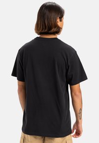 Camiseta de algodón negra con mangas cortas y cuello redondo clásico. Presenta un corte relajado y una textura suave. Diseño simple sin gráficos.