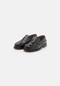 Mocassins en cuir noir avec une finition lisse, des coutures décoratives et un profil bas. Le design présente une bande sur le dessus.