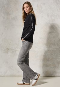 Schwarzes Langarmshirt mit weißen Seitenstreifen, kombiniert mit hellgrauen Jeans und weißen Sneakern mit schwarzen Akzenten. Glattes Material, lässige Passform.