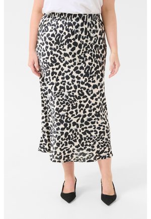 Vrouw draagt een midi-rok met zwart-witte luipaardprint, een witte top en zwarte puntige hakken, staand tegen een effen achtergrond.