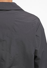 Mörkgrå skjorta med krage som har en slät, matt yta. Tyget verkar lätt och har en enkel, ren design utan synliga mönster.