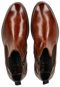 Bottines en cuir marron avec des panneaux latéraux élastiques, bout rond et coutures discrètes. Texture lisse avec fermeture éclair et languette de traction.