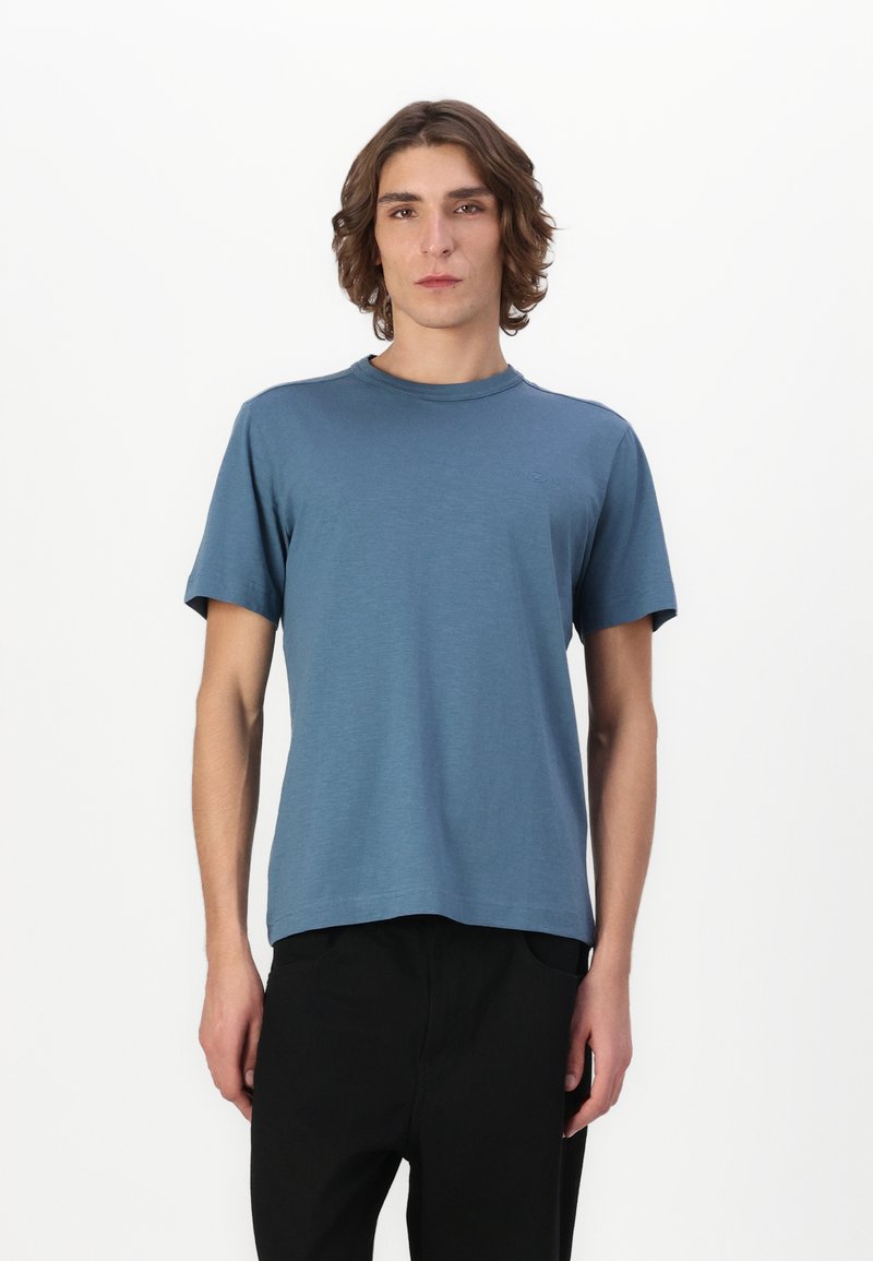Tricou albastru cu mânecă scurtă, fabricat dintr-un material moale, cu decolteu rotund și o croială lejeră; prevăzut cu un branding minim pe față.