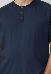 Granatowa koszulka henley z krótkim rękawem, wykonana z miękkiej tkaniny, z zaokrąglonym kołnierzykiem i trzema metalowymi guzikami na przodzie.